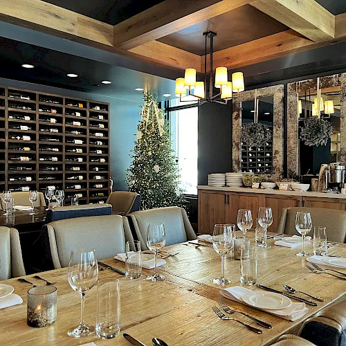 A restaurant dining room with a tall decorated Christmas tree, a chandelier, and walls packed with wine bottles.