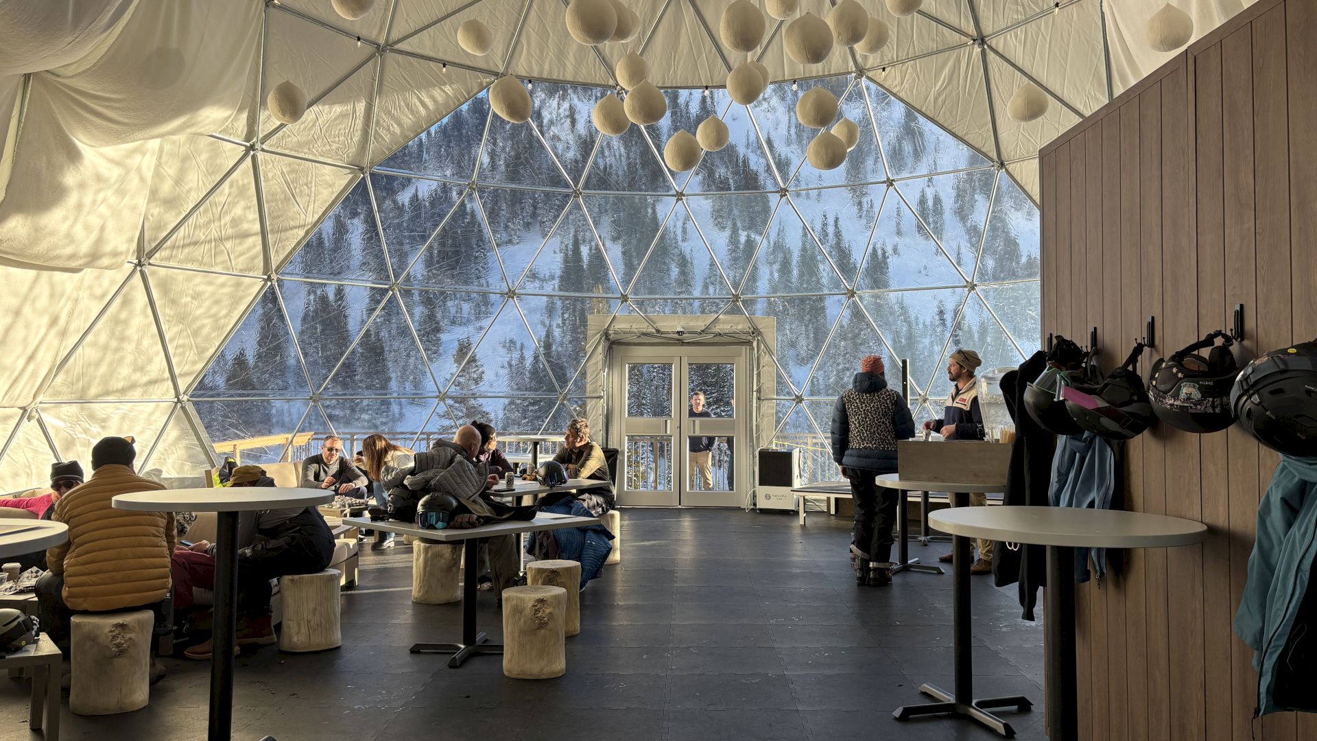 Inside a snow dome: guests relax in a geodesic tent, helmets on, while a speaker stands by the front desk.