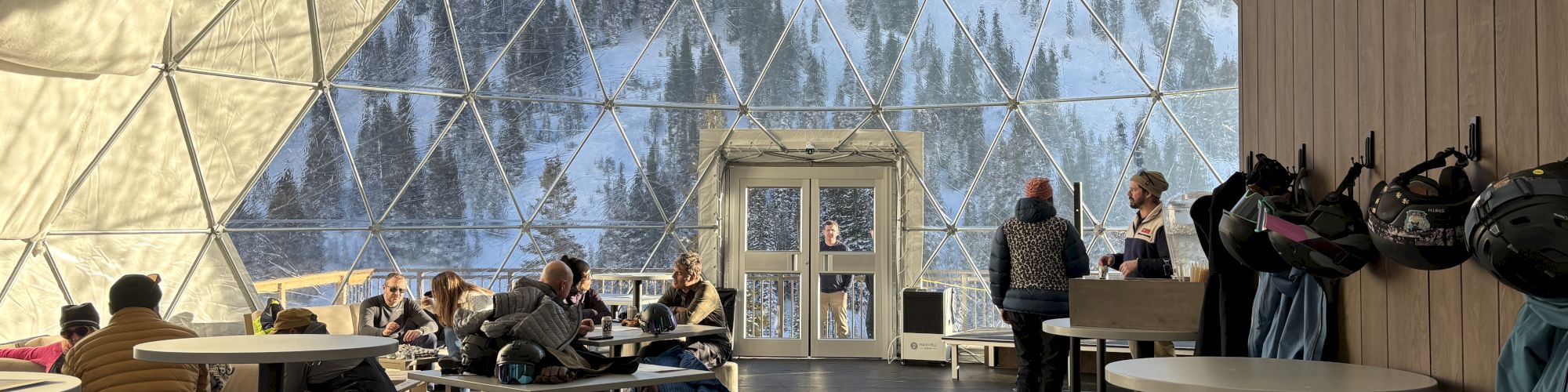 Inside a snow dome: guests relax in a geodesic tent, helmets on, while a speaker stands by the front desk.