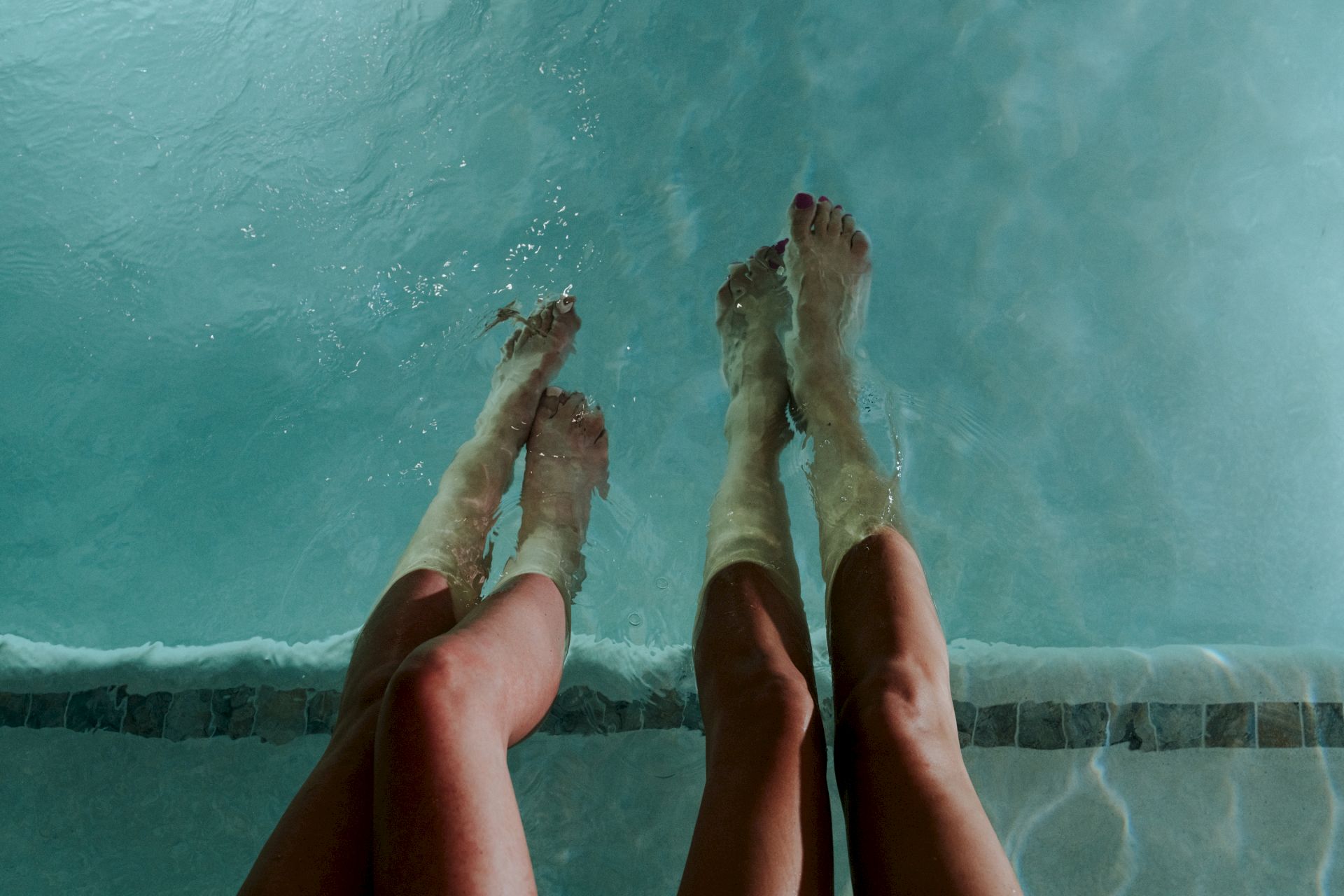 Bare feet in a swimming pool splashing water, toes pointed up as if relaxing by the edge.
