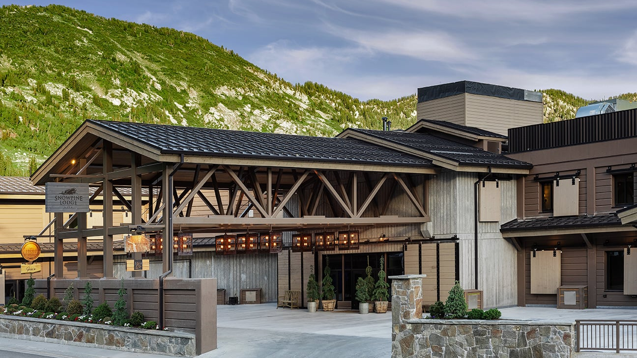 A mountain lodge with timber beams, stone base, and a dark metal roof under clear skies.