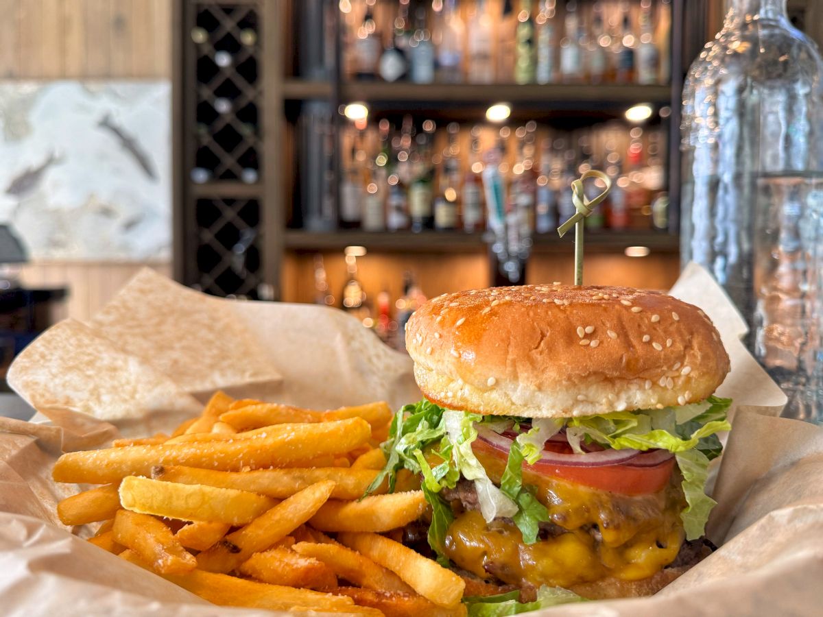 A cheeseburger with fries on a tray in a restaurant, with a small yellow ribbon on top as lights blur in the background.