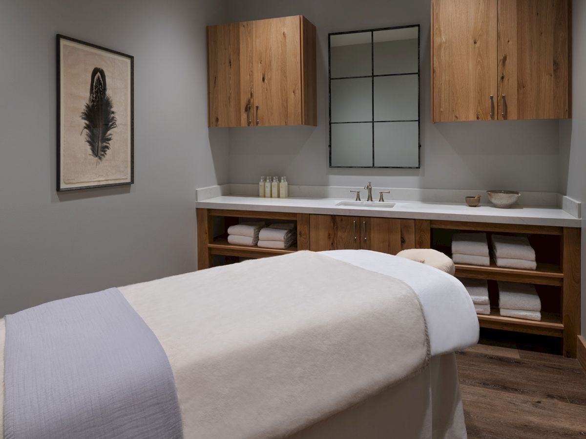 A modern bathroom suite with a double vanity, wall cabinets, a lit mirror, neatly folded towels, toiletries, and framed feather art.