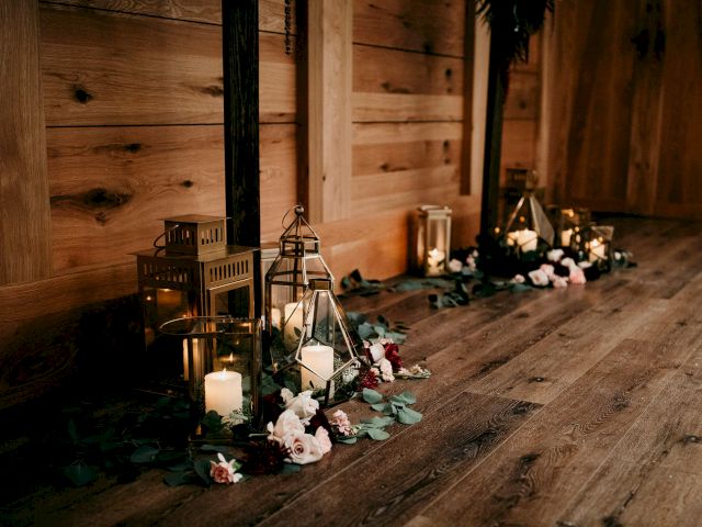 Wooden indoor aisle lined with lit lantern candles and scattered flowers, creating a warm event glow.