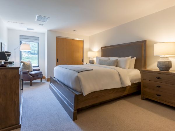 A modern bedroom featuring a large neatly made bed, bedside tables and lamps, and large windows with a scenic view.