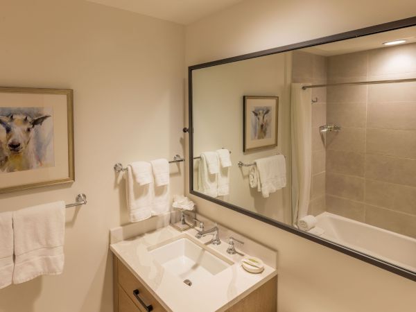 A modern bathroom with a white vanity, chrome faucet, large mirror, folded towels, framed art, and a glass shower.