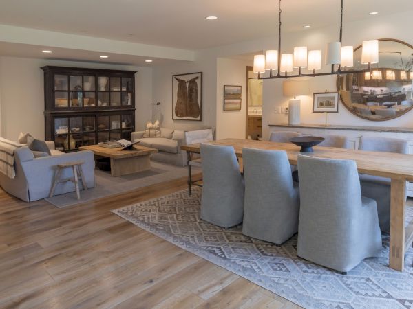 A modern living/dining room with sofas, wooden table, pendant lights, and a mirrored wall over a bar area.