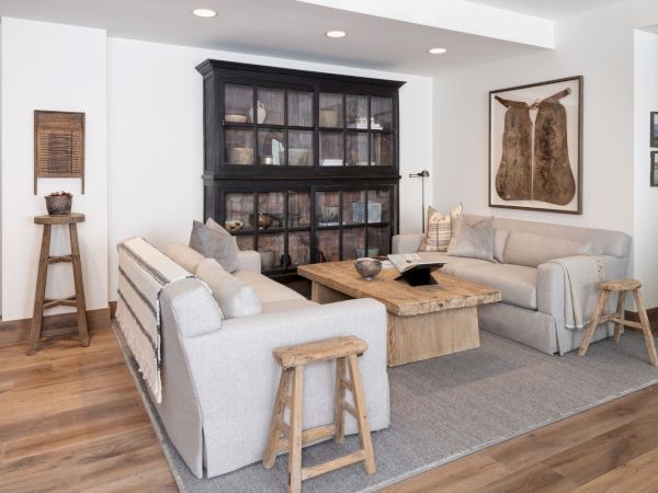 A cozy living room with a light sofa, rustic coffee table, dark glass cabinet, and framed wall art.