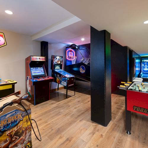 An arcade game room with pinball and foosball/air-hockey tables, plus neon-lit VR screens and a &ldquo;Skee-Ball&rdquo; machine.