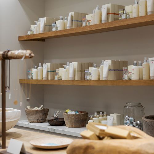 A bright beauty shop display shows shelves stocked with skincare bottles, boxed products, bowls, and grooming supplies on a counter.