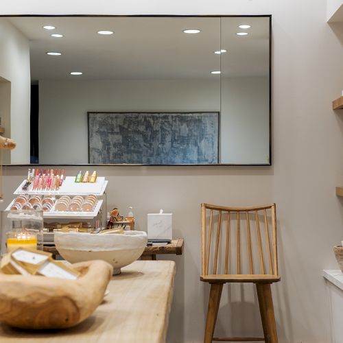 A bright salon-spa counter with a wooden chair, skincare product bottles, and a display of creams behind glass.