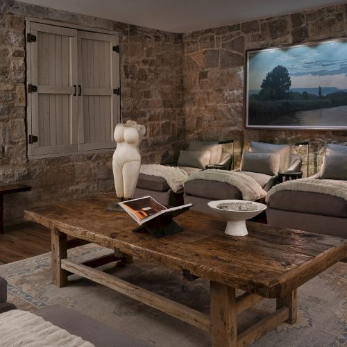 Rustic living room with stone walls, shuttered door, sofas, a large landscape photo, and a wooden coffee table.
