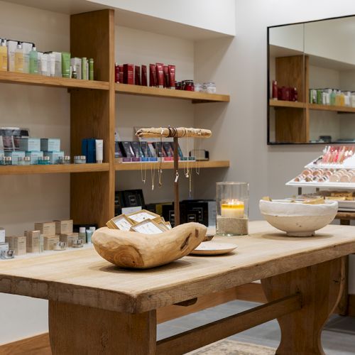 A spa shop interior with a rustic wooden display table, candles, and shelves of toiletries and gift items.