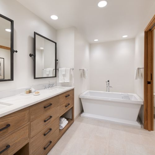 Modern bathroom with dual sinks, large mirrors, towels, and a built-in bathtub and shower head.