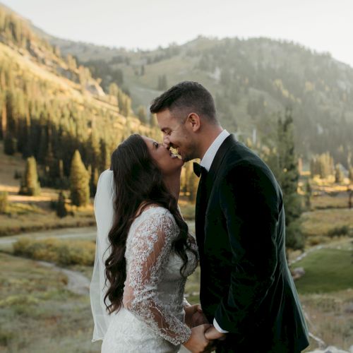 Wedding couple in a scenic mountain valley, standing close and kissing as golden light fills the background hills.