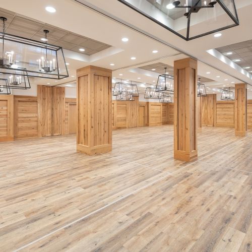 A bright modern hall with wooden pillars and paneling, polished wood floors, and hanging lantern-style lights.