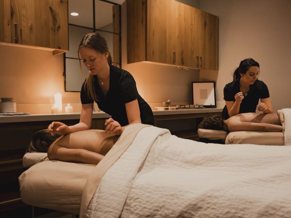 A massage therapist performs a relaxing massage on a client lying on a bed in a warm spa room.