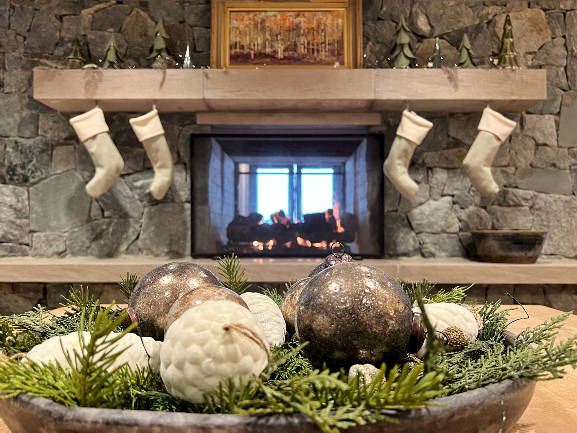 A cozy stone fireplace decorated for Christmas with hanging stockings and shiny ornaments in a glowing hearth.
